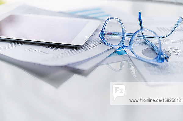 Blue eyeglasses and tablet on business papers