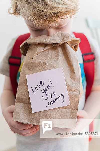 Boy (4-5) peeking into lunch bag with note from mom