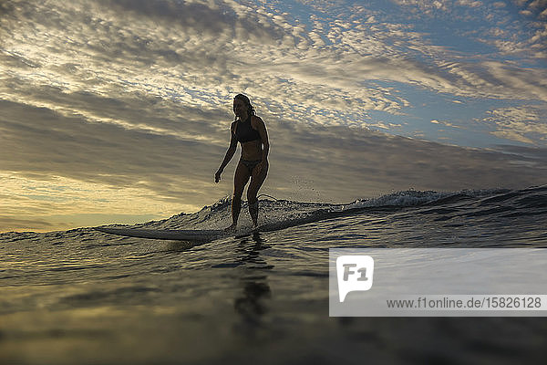 Junge Frau surft bei Sonnenaufgang