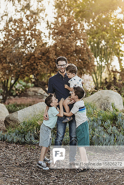 Portrait of dad holding three sons and smiling in sunny cactus garden