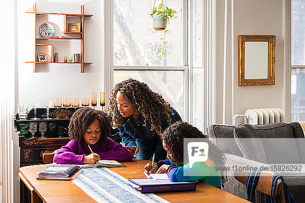 Mutter hilft der Tochter bei den Hausaufgaben bei Tisch im Wohnzimmer