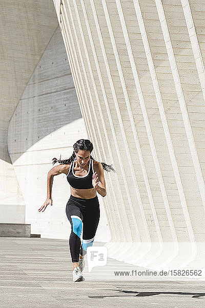 Ganzkörper einer Sportlerin in Sportkleidung  die auf Beton läuft