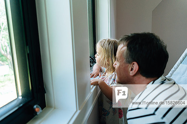 Seitenansicht eines Vaters und einer Tochter  die auf ein Fenster schauen