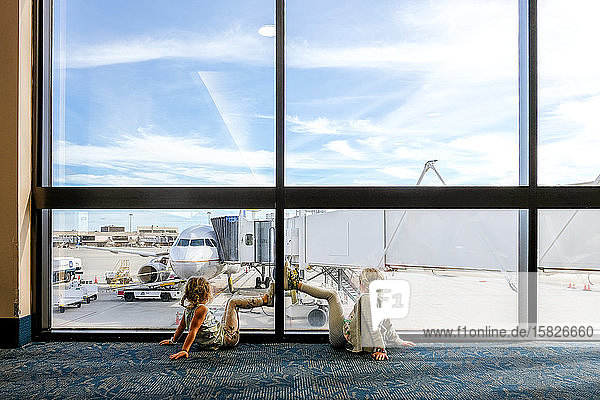 two girls sitting on floor in airport staring at airplane waiting