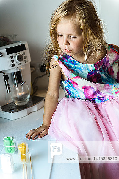 Kleines Mädchen in elegantem Kleid  das auf einem Tisch in der Küche sitzt