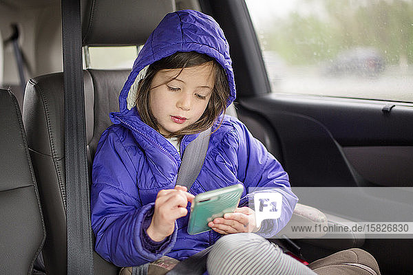 Ein Kleinkind sitzt auf einer Reise in seinem Autositz und spielt mit einem Mobiltelefon
