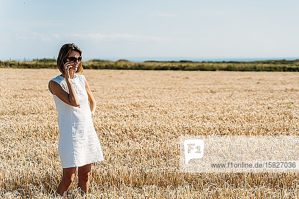 Cheerful woman is talking on the phone in the golden grass field.