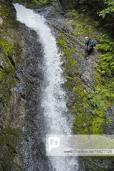 Seitenansicht eines Mannes  der sich neben einem Wasserfall im Canyon abseilt.