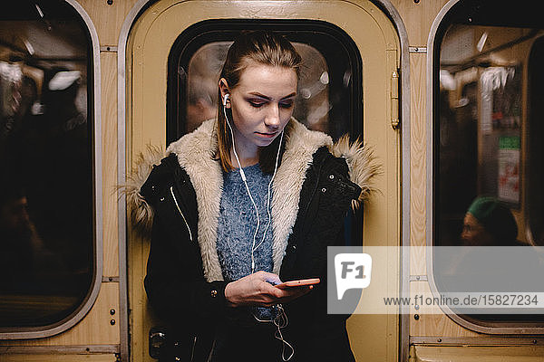 Junge Frau benutzt Smartphone während der Fahrt in der U-Bahn