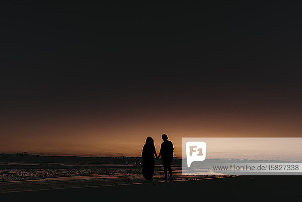 Silhouette von Mann und Frau beim Spaziergang am Strand bei Sonnenuntergang