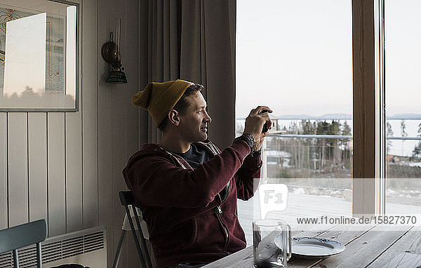 Mann  der die Aussicht von seinem Balkon zu Hause in Schweden fotografiert