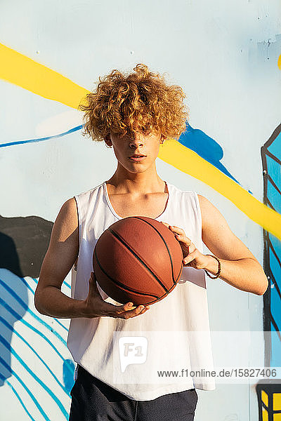 Young men with curvy hairs holding basketball ball while standing on a street
