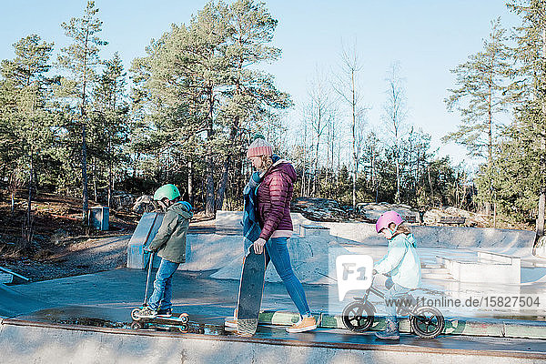 Mama und ihre Kinder laufen über einen Skatepark  um zu fahren und Spaß zu haben