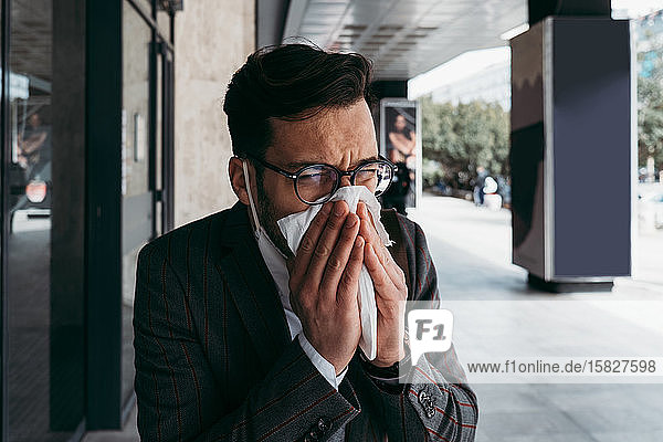 Kranker Mann mit schützender Gesichtsmaske hustet und niest auf der Straße.