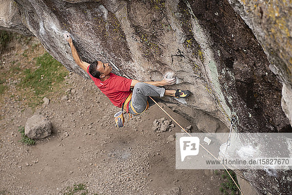 One man wearing red hold himself while rock climbing in Jilotepec