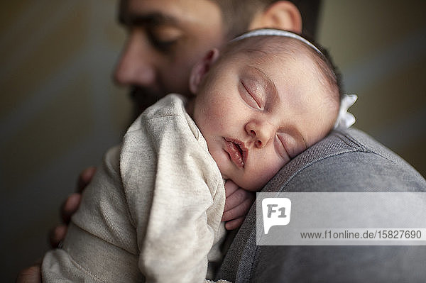 Close up of newborn baby's face sleeping on father's shoulder at home