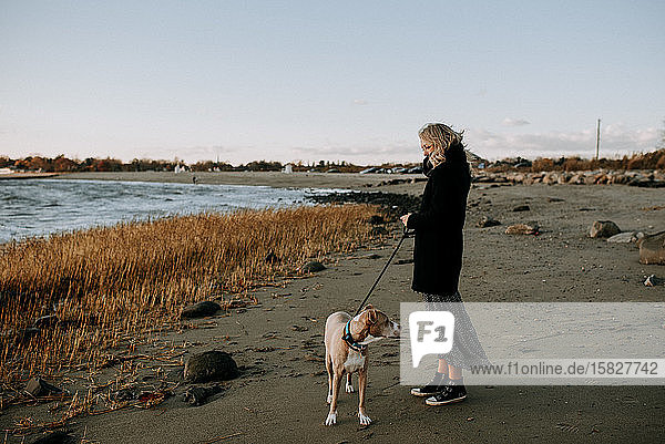 Frau steht im Winter mit Hund am Strand