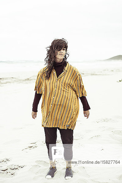Natürliches Mädchen steht am windigen  abgelegenen Strand mit übergroßem Hemd