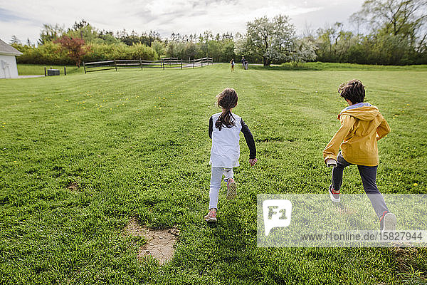 Three children run through a field at springtime  one far ahead