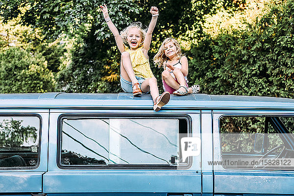 two girls happy and excited sitting on top of vintage car