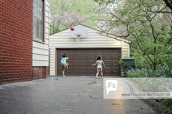 Ein Junge springt in die Einfahrt  um einen Basketball zu schießen  während die Schwester zuschaut