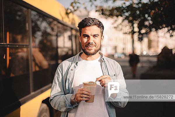 Happy man holding cup of coffee while standing on street during summer