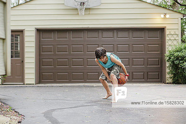 Ein barfüssiger Junge dribbelt in der Dämmerung in seiner Auffahrt einen Basketball