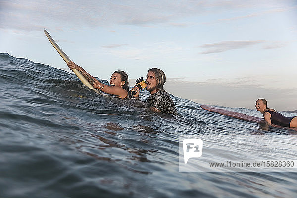 Glückliche Freunde mit Surfbrettern und Kamera im Meer