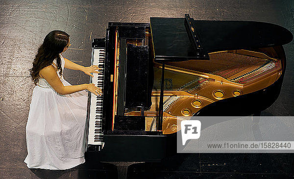 Eine Frau mit braunem Haar in einem weißen Kleid  die auf einem schwarzen Flügel mit erhobenem Deckel spielt. Blick von oben auf den Pianisten