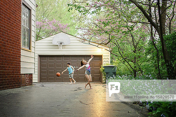 Ein kleines Mädchen tanzt barfuss  während der Bruder hinten Basketball spielt