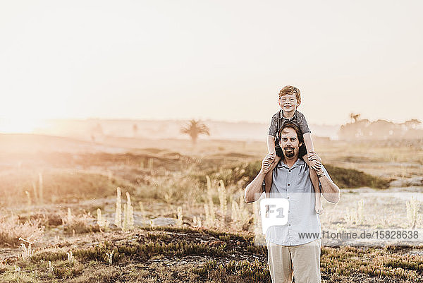 Father holding son up on shoulders while smiling at camera at beach