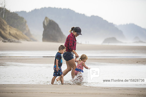Seitenansicht einer Mutter  die mit ihren zwei kleinen Kindern am Strand spazieren geht.