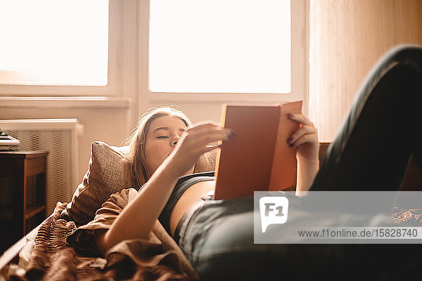 Teenage girl reading book while lying on bed at home