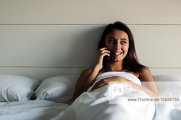Junges und schönes Mädchen ruft mit dem Handy im Bett an.