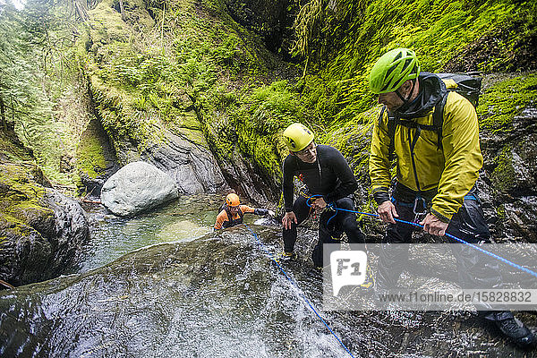 Drei abenteuerlustige Männer arbeiten als Team  um einen Freund am Wasserfall zu sichern.