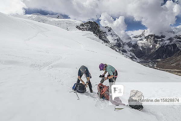 Two women mountaineers take a gear break on the Mera Peak glacier