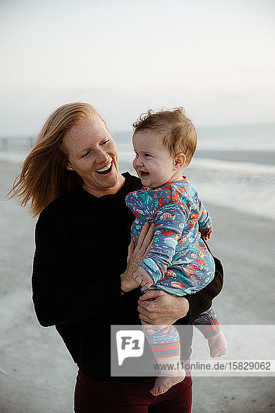 young mother and healthy chubby boy child smile during beach walk