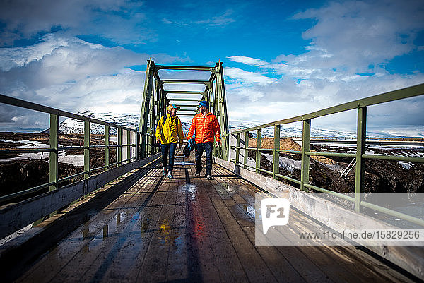 Mann und Frau in Jacken gehen in Island über die Brücke