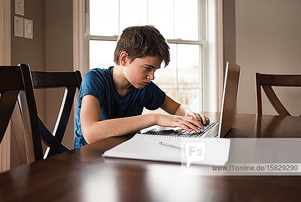 Tween boy working on his homework on a laptop commuter at home.