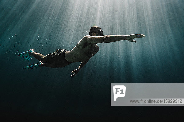 Ein Mann in voller Länge  der im Ozean unter Wasser schwimmt