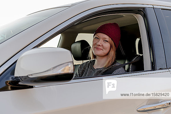 Frau lächelt bei Sonnenuntergang aus dem Auto in die Kamera