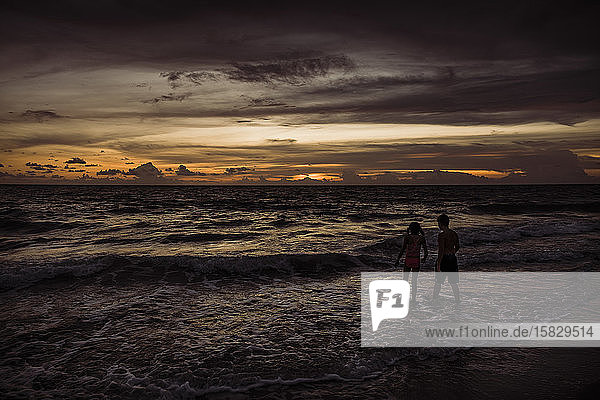 Zwei Kinder gehen bei Sonnenuntergang im Meer spazieren