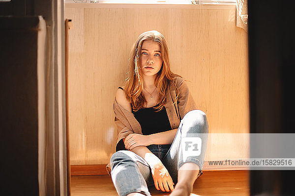 Süße junge Frau  die im Sommer auf dem Boden auf dem Balkon sitzt