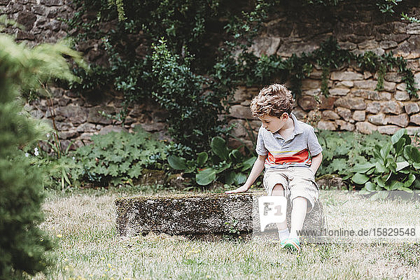 Front view of boy sitting on moss-covered rock-bench