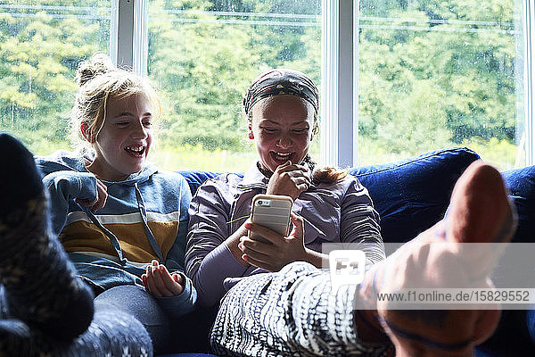 Teen girls laughing on a couch looking at something on a phone