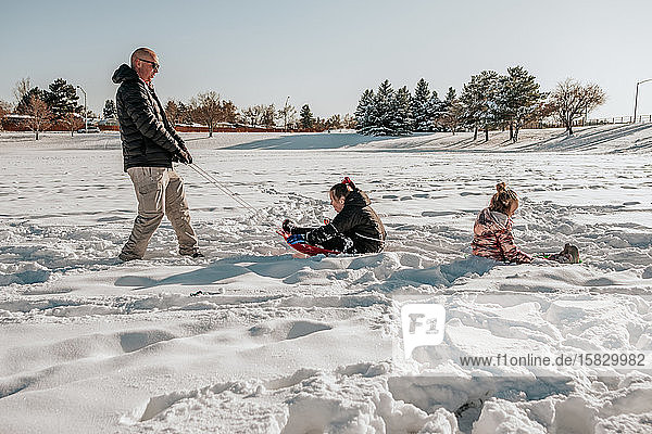 Side view of man pulling two girls on sled through field in winter