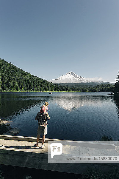 A father carries his daughter on his shoulders at Trillium Lake  OR.