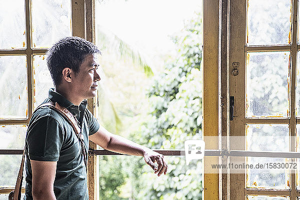Porträt eines Thailänders  der vor einem offenen Fenster steht