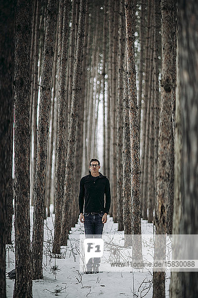 junger Mann steht aufrecht inmitten eines schneebedeckten Kiefernwaldes in Maine