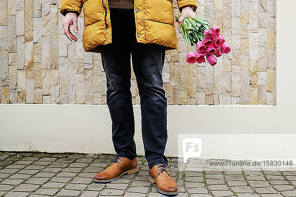 blond man in a yellow winter jacket with a bouquet of tulips in hands